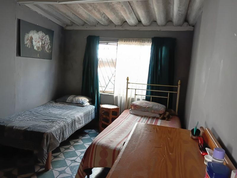 A bedroom featuring exposed corrugated ceiling panels, patterned floor tiles, and a window fitted with security bars.