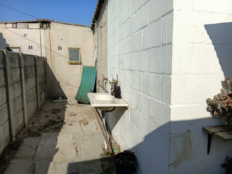 Rear exterior area featuring concrete block walls, basic paving, and an external utility sink.