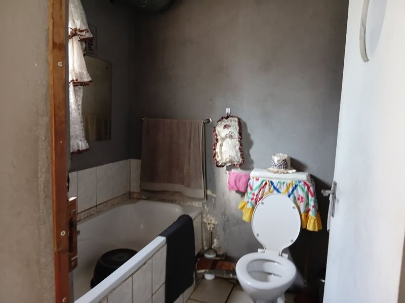 A compact bathroom featuring a bathtub and toilet, currently requiring significant wall repairs and cosmetic updates to improve the overall finish.