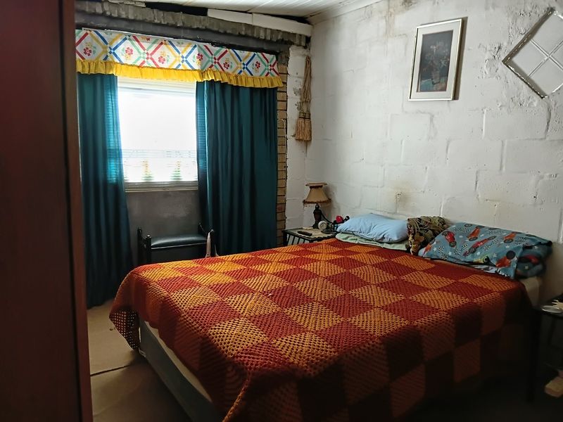 A bedroom featuring exposed brick walls and exposed ceiling beams, requiring cosmetic updates and finishing to improve the overall aesthetic and condition.