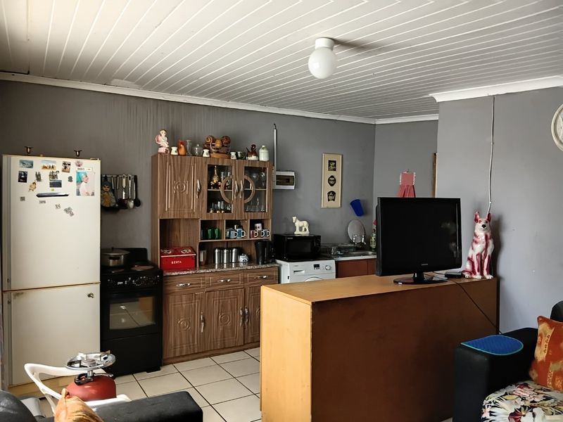 Open plan living and kitchen area featuring tiled floors, wood-look cabinetry, and a tongue and groove ceiling, showing signs of wear and wall staining.