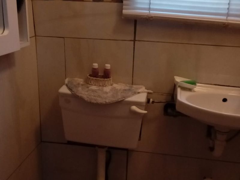 A compact bathroom featuring a wall-mounted basin, toilet, and tiled walls with a decorative border.