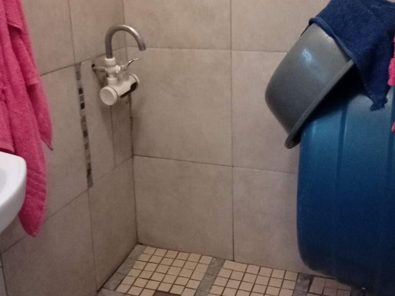 A bathroom shower area featuring tiled walls and flooring, currently showing significant wear and damage to the floor tiles requiring repair.