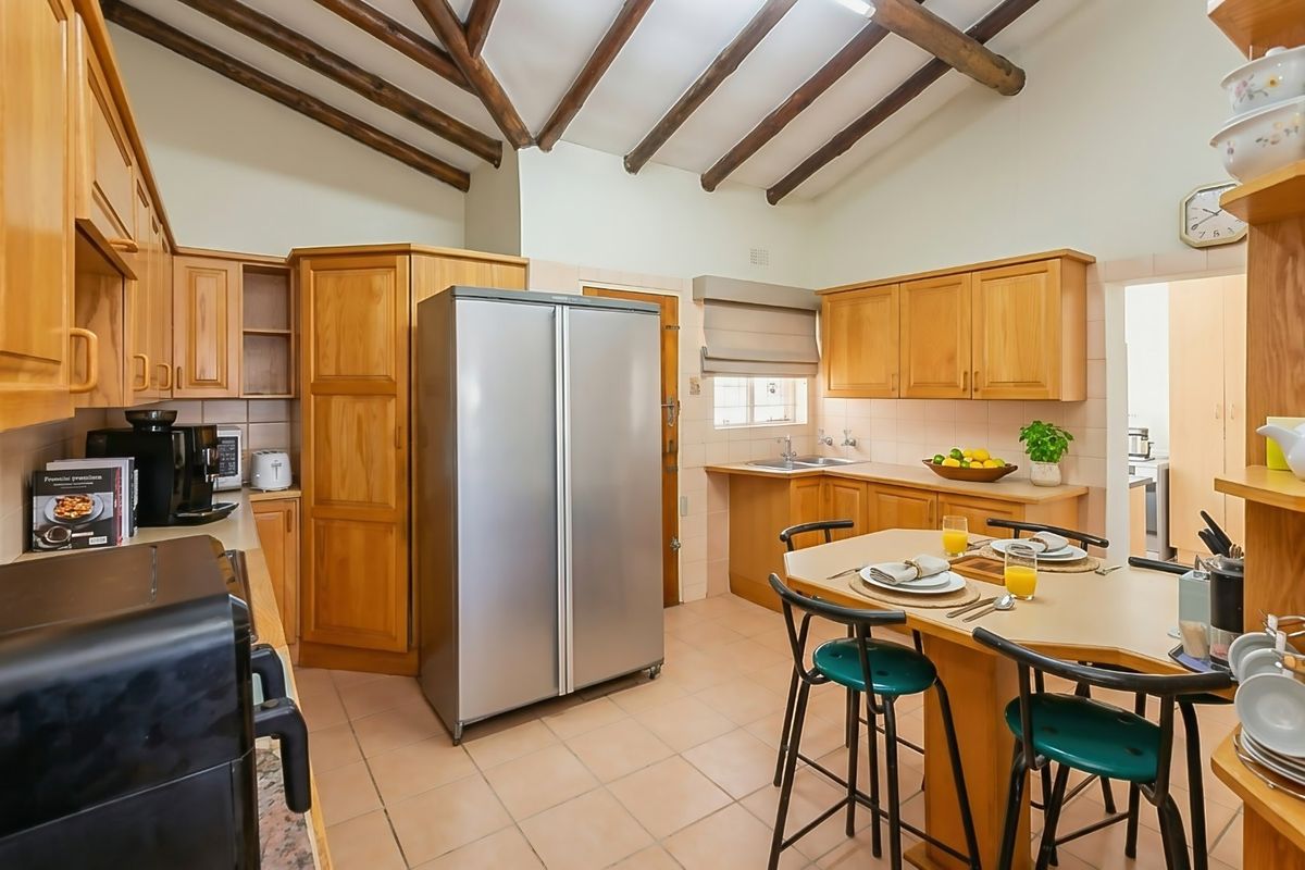 A functional kitchen featuring warm wooden cabinetry, exposed timber ceiling beams, tiled flooring, and a convenient breakfast nook area.