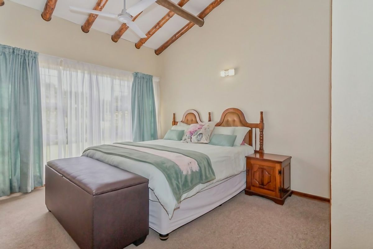 A comfortable bedroom featuring exposed timber ceiling beams, a ceiling fan, and neutral wall finishes, providing a warm and inviting atmosphere.