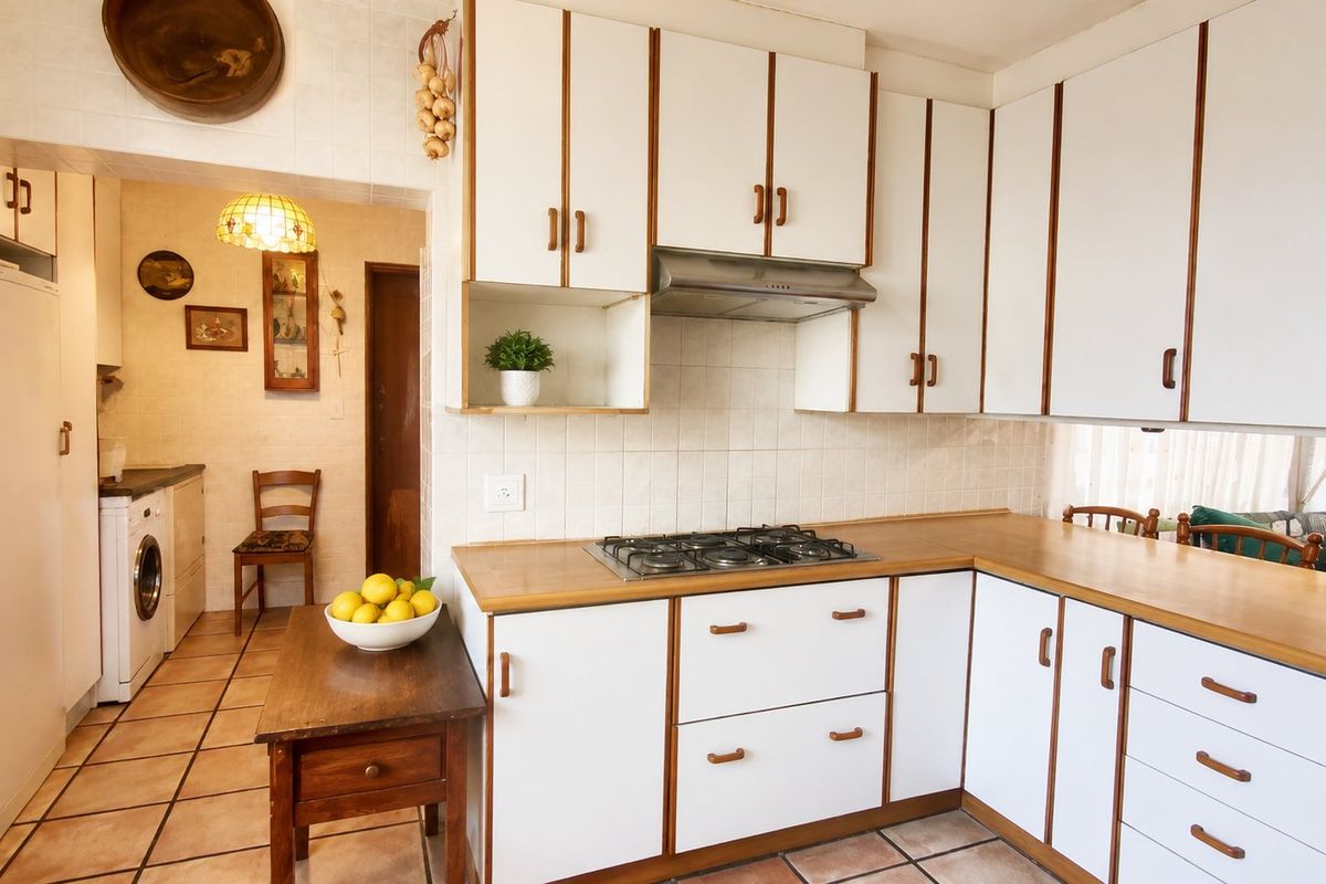 A functional kitchen featuring white cabinetry with wood trim, a gas cooktop, extractor fan, and tiled flooring, with an adjacent laundry area.