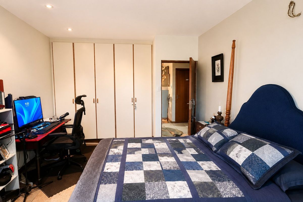 A functional bedroom featuring built-in wardrobes, recessed downlighting, and direct access to an adjoining hallway.