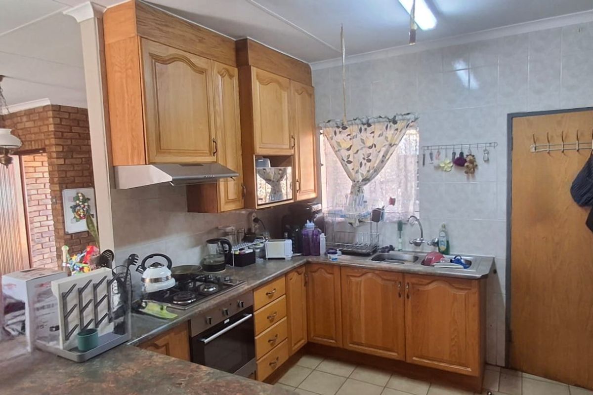A functional kitchen featuring wooden cabinetry, laminate countertops, a built-in oven with gas hob, and tiled splashbacks, adjacent to an open-plan living area.
