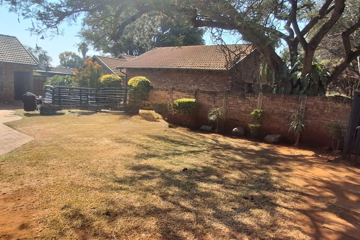 A rear garden area featuring a paved patio, brick boundary wall, and established trees, providing a private outdoor space.