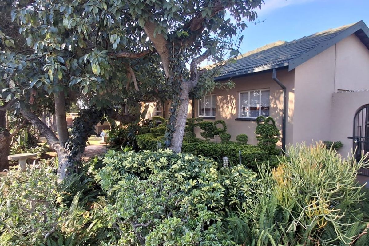 A view of the rear exterior of the house featuring a landscaped garden, mature trees, and a paved pathway leading to a secure gated entrance.