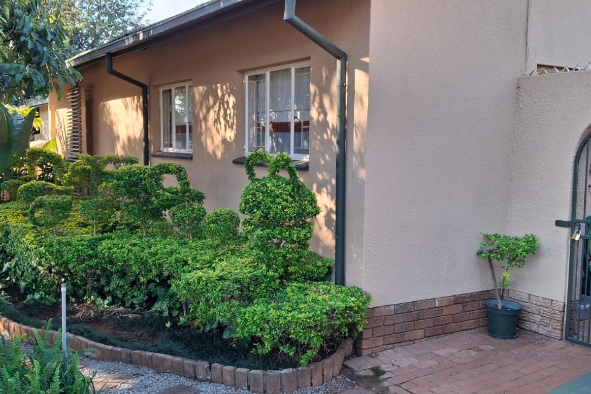 A well-maintained rear exterior view featuring a paved walkway, landscaped garden beds, and a secure metal gate entrance.