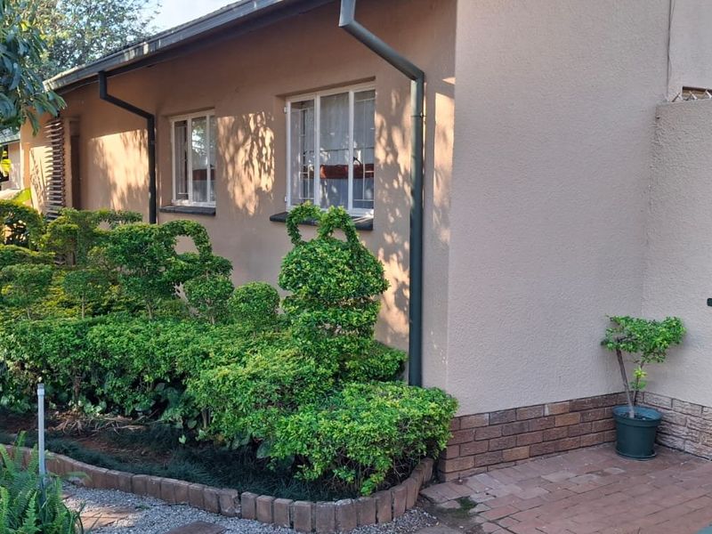 A well-maintained rear exterior view featuring a paved walkway, landscaped garden beds, and a secure metal gate entrance.