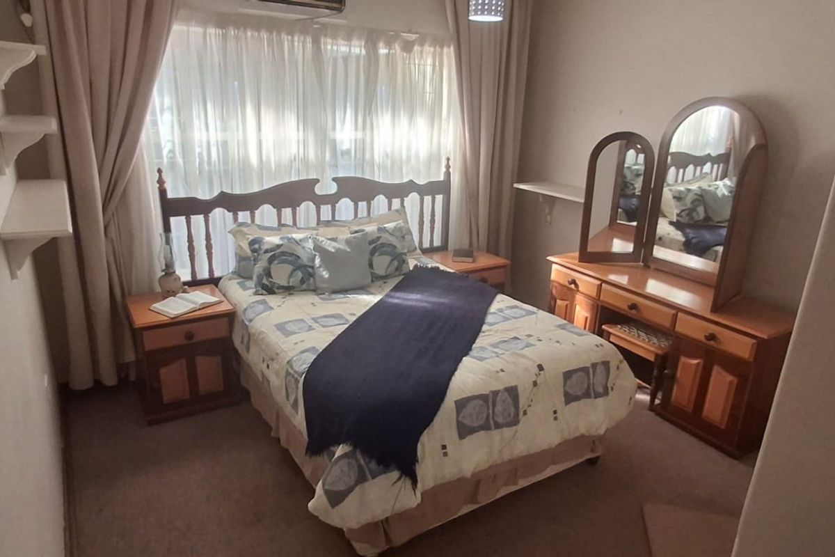 A standard bedroom featuring wall-mounted shelving, carpeted flooring, and an integrated air conditioning unit.