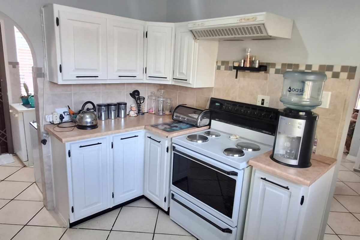 A functional kitchen featuring white cabinetry, laminate countertops, a freestanding electric stove with extractor fan, and tiled flooring throughout.