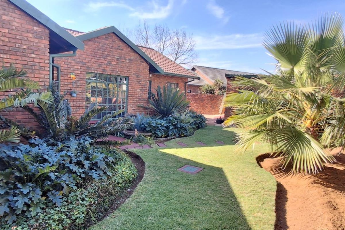 A well-maintained rear garden featuring a face brick facade, established landscaping, and a paved pathway leading along the side of the house.