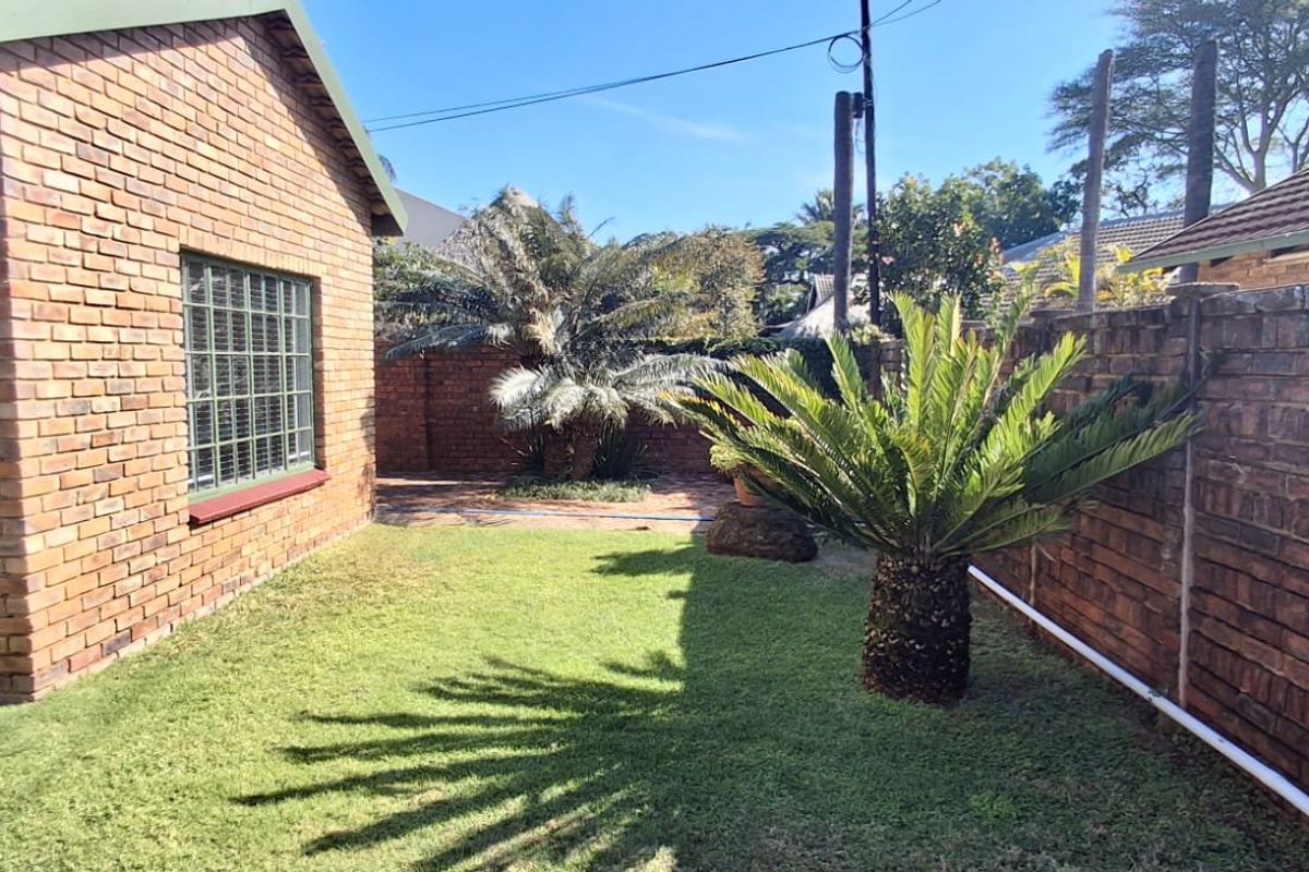 A private rear garden area featuring a well-maintained lawn, face brick exterior walls, and secure brick boundary fencing.
