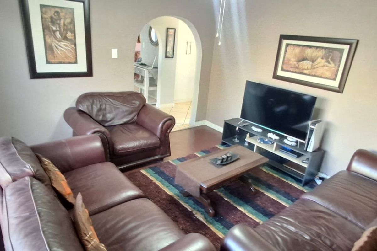 A cozy living room featuring laminate flooring, an arched doorway leading to an adjacent space, and large windows with venetian blinds.
