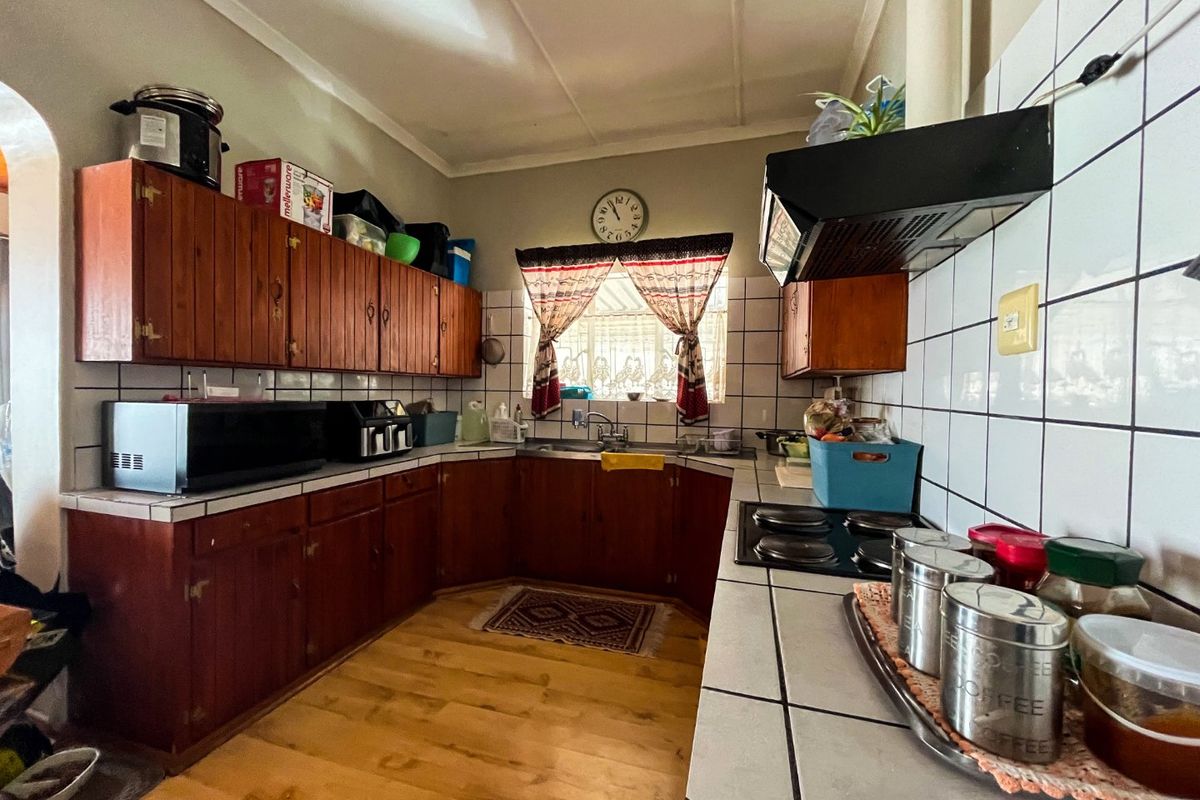 A functional kitchen featuring wooden cabinetry, tiled backsplash, built-in electric hob, and extractor fan, offering a classic layout with potential for modern updates.