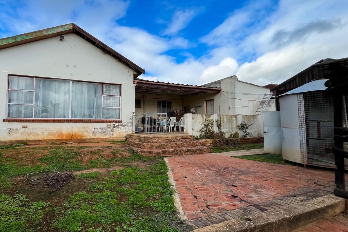 Rear view of the property featuring a covered patio, brick paved area, and visible exterior wall maintenance requirements.