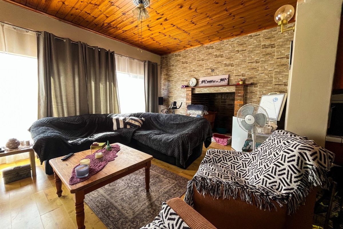 Living room featuring a stone accent wall, brick fireplace, and timber ceiling, providing a rustic aesthetic with laminate flooring throughout.