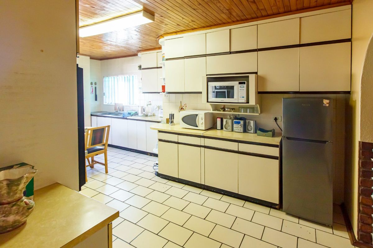A dated kitchen featuring extensive built-in cabinetry, tiled flooring, and a timber-paneled ceiling, offering significant potential for a modern renovation.