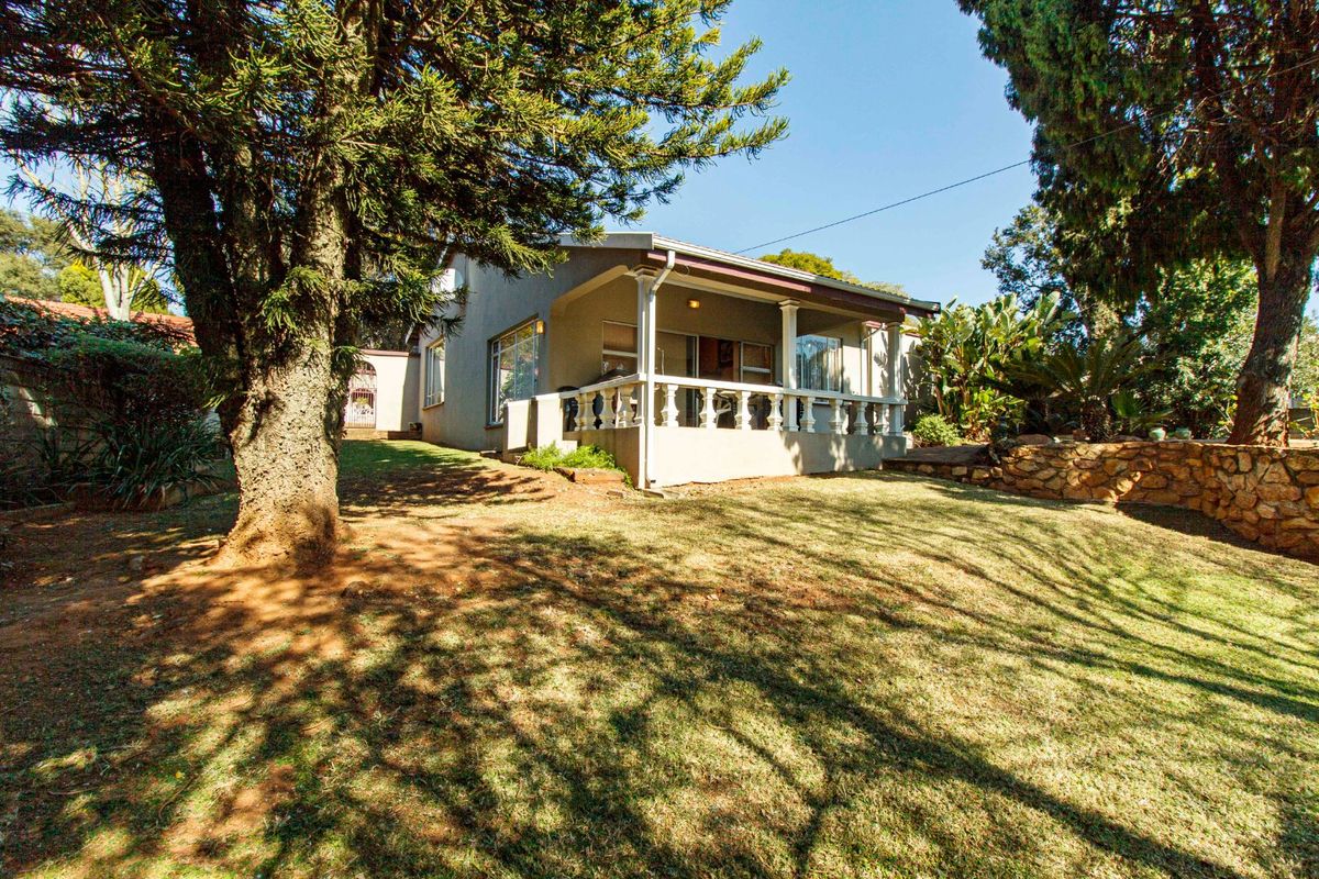 A view of the rear exterior of the house featuring a covered patio with a balustrade, set within a landscaped garden with stone retaining walls.