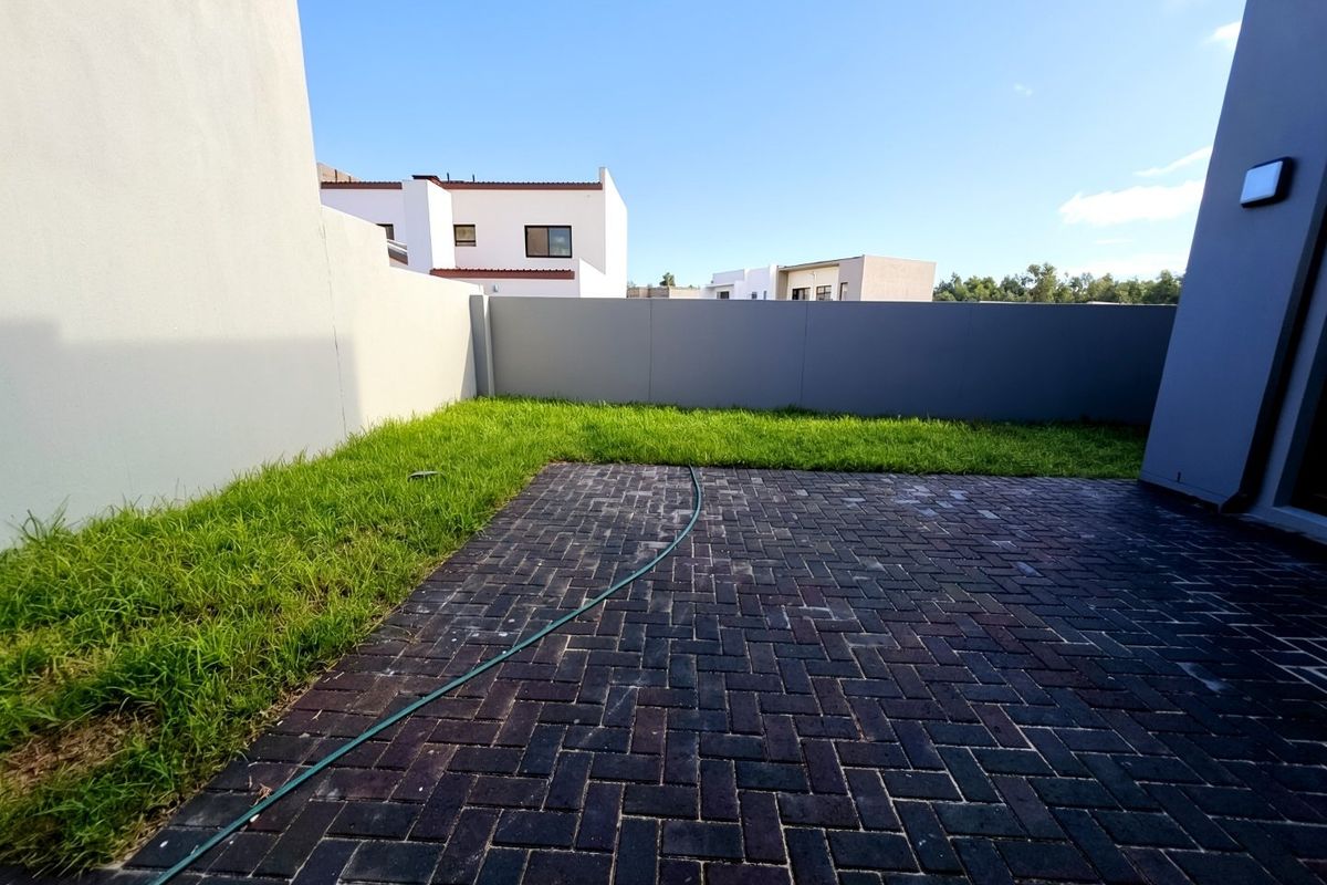 A private rear courtyard featuring a paved patio area and a small lawn, enclosed by modern boundary walls.