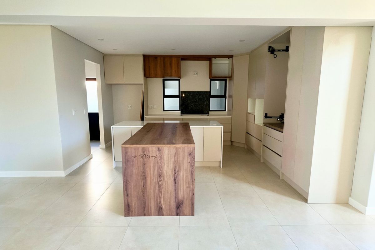 Modern, spacious kitchen featuring a central island, ample built-in cabinetry, and neutral tiled flooring, currently awaiting final appliance installation and finishing touches.