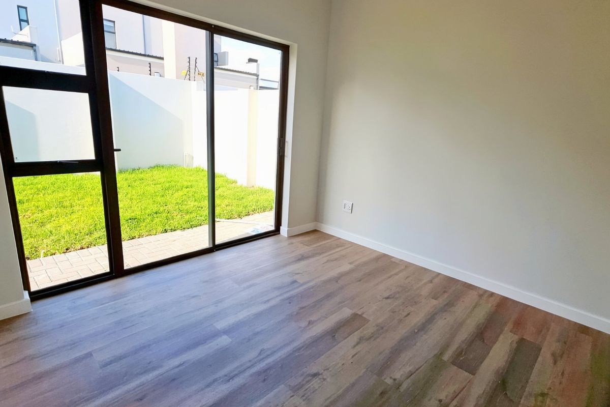 A bright, empty bedroom featuring modern laminate flooring and a large sliding glass door providing direct access to a private garden area.