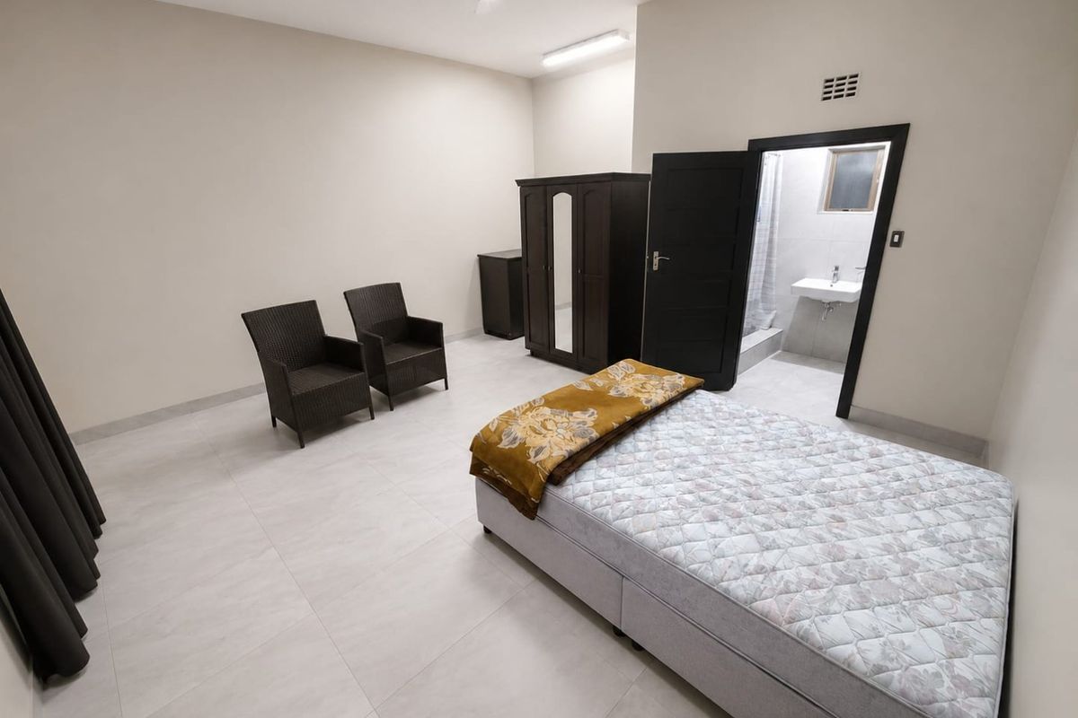 Spacious bedroom featuring neutral tiled flooring and an attached en-suite bathroom, offering a clean and functional living space.