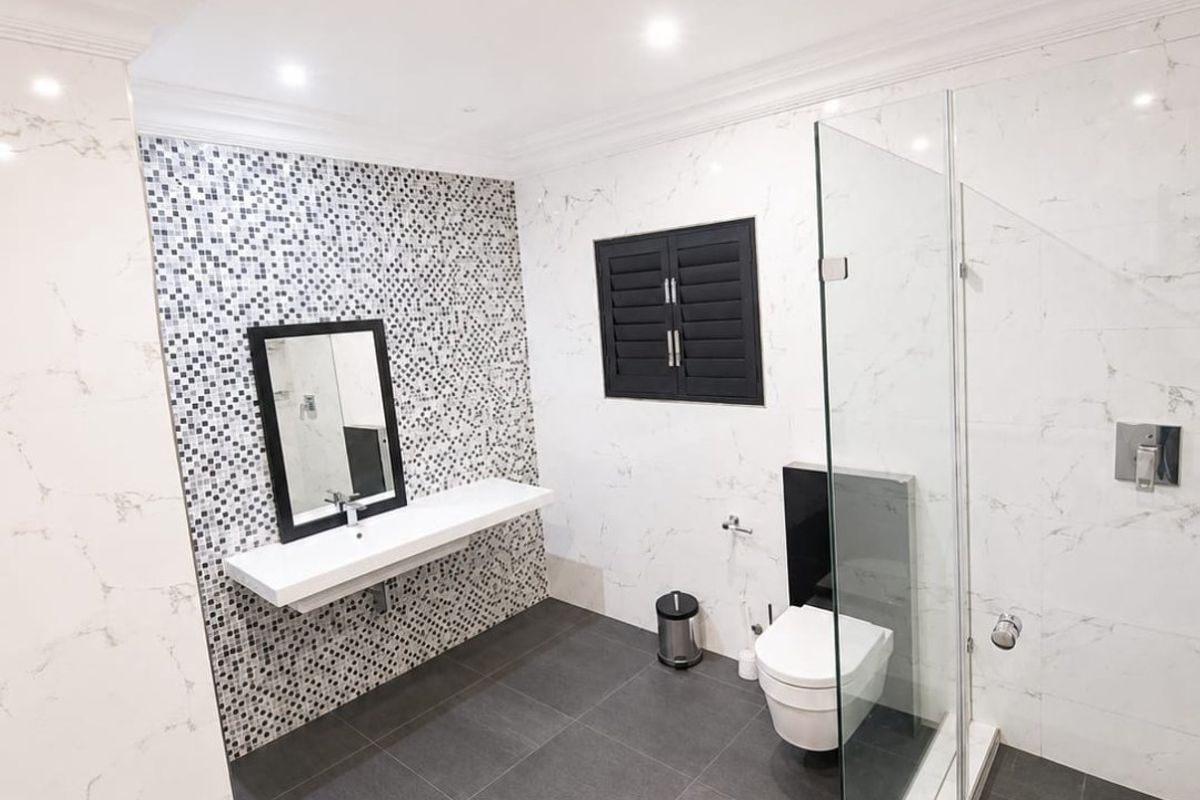 Modern bathroom featuring a floating vanity, wall-mounted toilet, glass-enclosed shower, and elegant marble-look wall tiles with a mosaic feature wall.