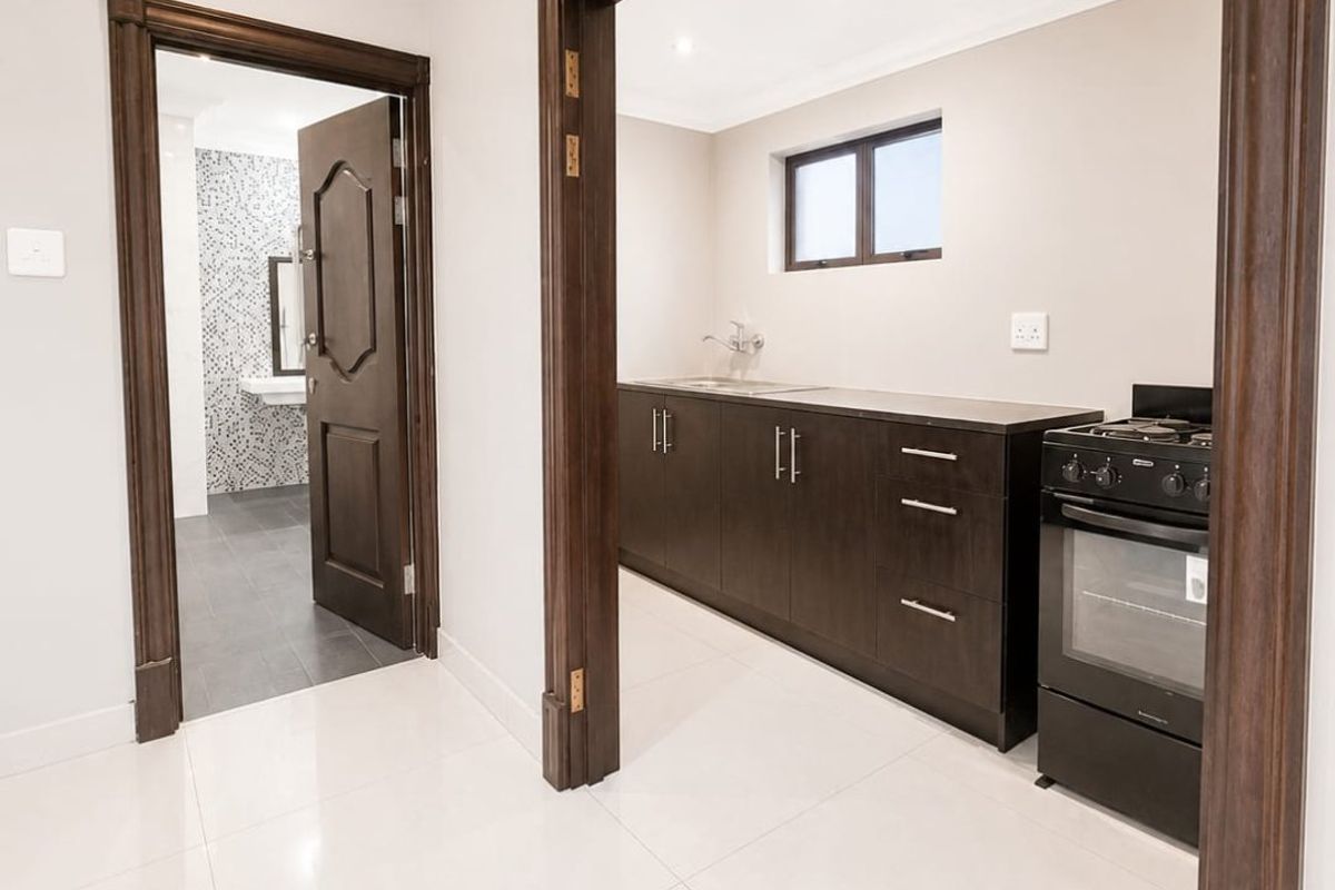 A clean, modern kitchen area featuring dark wood cabinetry, built-in oven, and sleek tiled flooring, with an adjacent view into a tiled bathroom.