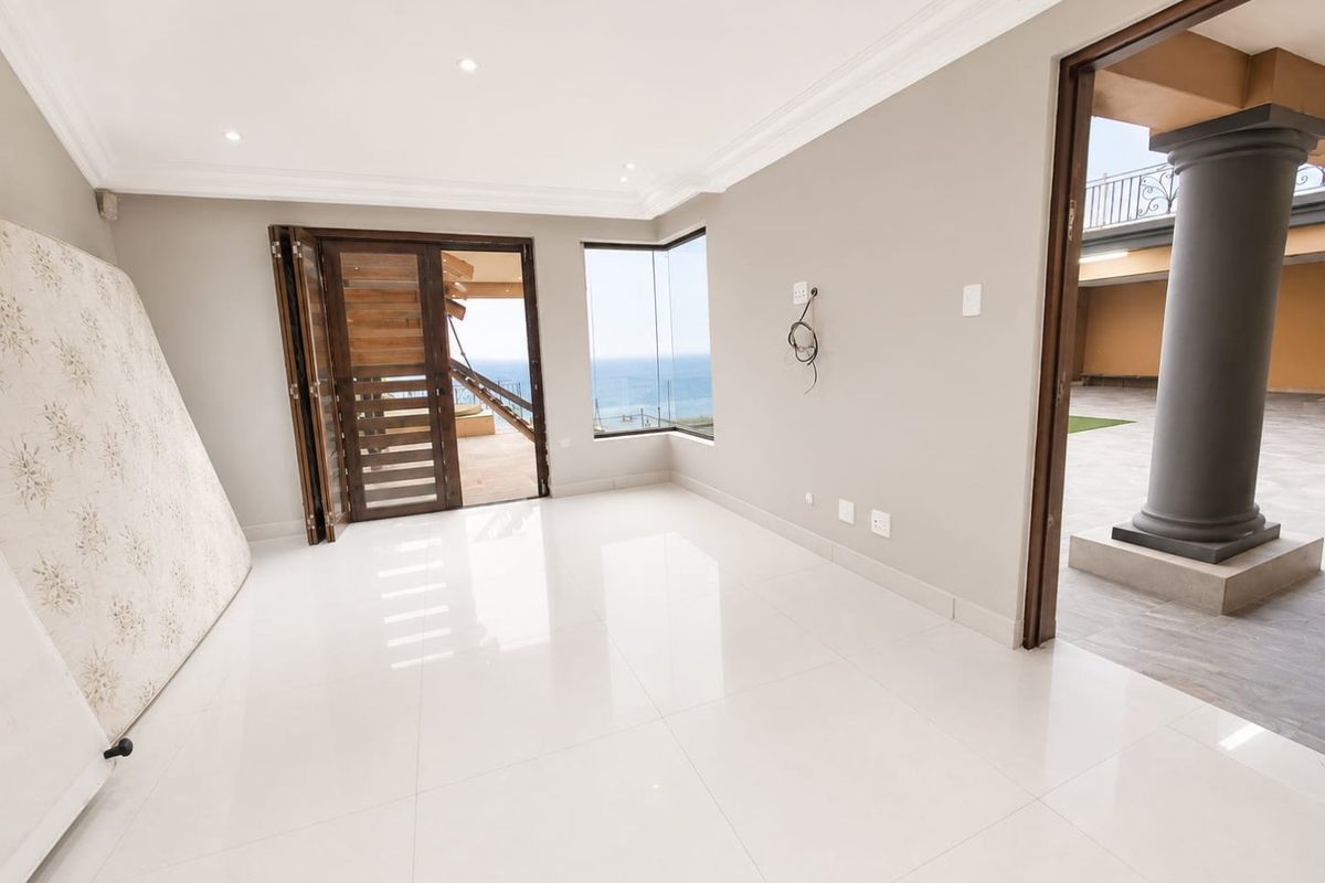 A bright, empty living area featuring polished porcelain tiles, recessed lighting, and bi-fold doors leading to an outdoor patio with ocean views.