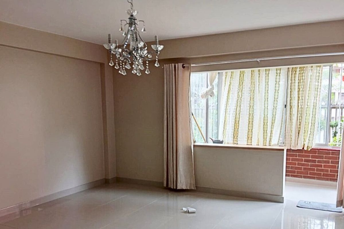 A spacious, empty living room featuring tiled flooring, a decorative crystal chandelier, and large windows providing natural light and access to a balcony.