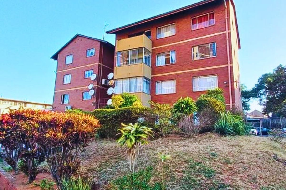 Exterior view of a multi-story brick apartment building featuring enclosed balconies and established garden landscaping.
