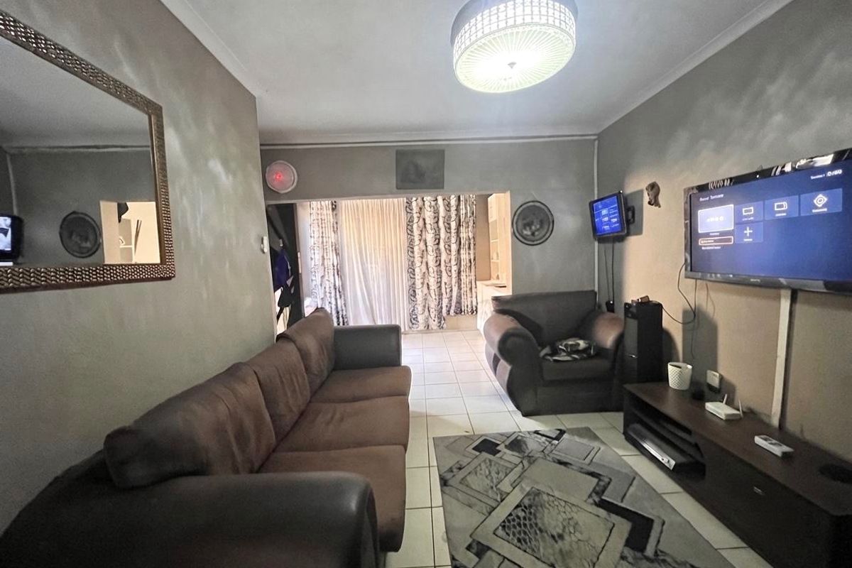 A living room featuring tiled flooring and wall-mounted television, with access to an adjacent area through a wide opening.