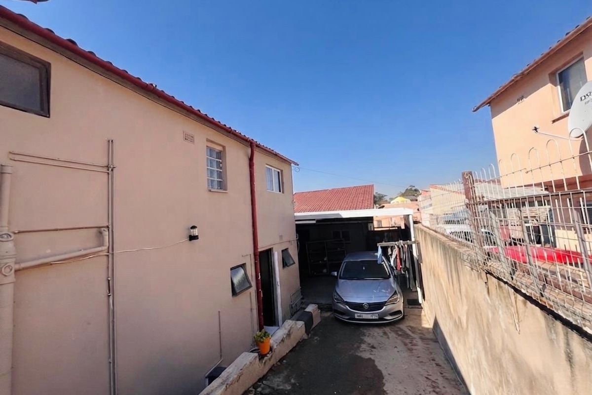 Rear exterior view of the property featuring a concrete driveway, security fencing, and multi-level building structure with tiled roofing.