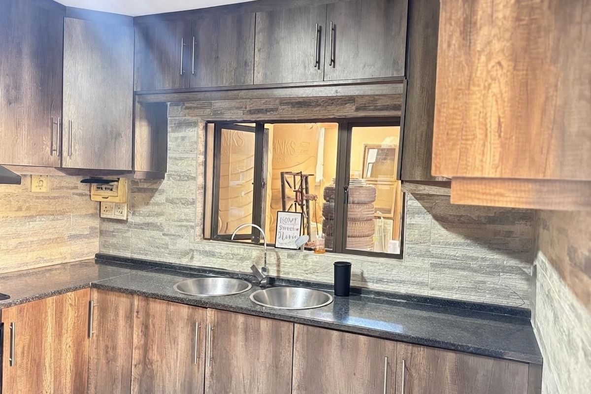 A functional kitchen featuring dark wood-look cabinetry, granite countertops, a double sink, and a textured stone veneer backsplash.