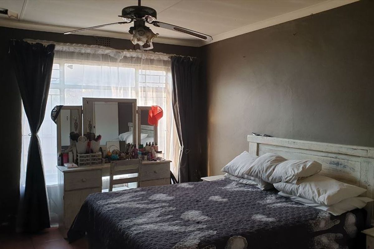 A bedroom featuring tiled flooring and a ceiling fan, currently showing signs of wear including ceiling damage and exposed wiring.