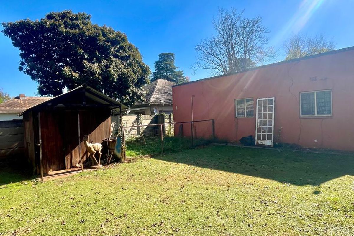 Rear garden area featuring a lawn, a timber storage shed, and the rear elevation of the house with visible exterior wall finishes.
