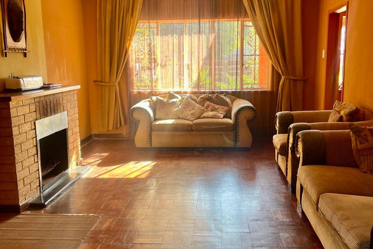 A living room featuring traditional parquet flooring, a brick fireplace, and a central chandelier, offering a dated aesthetic with potential for modernization.