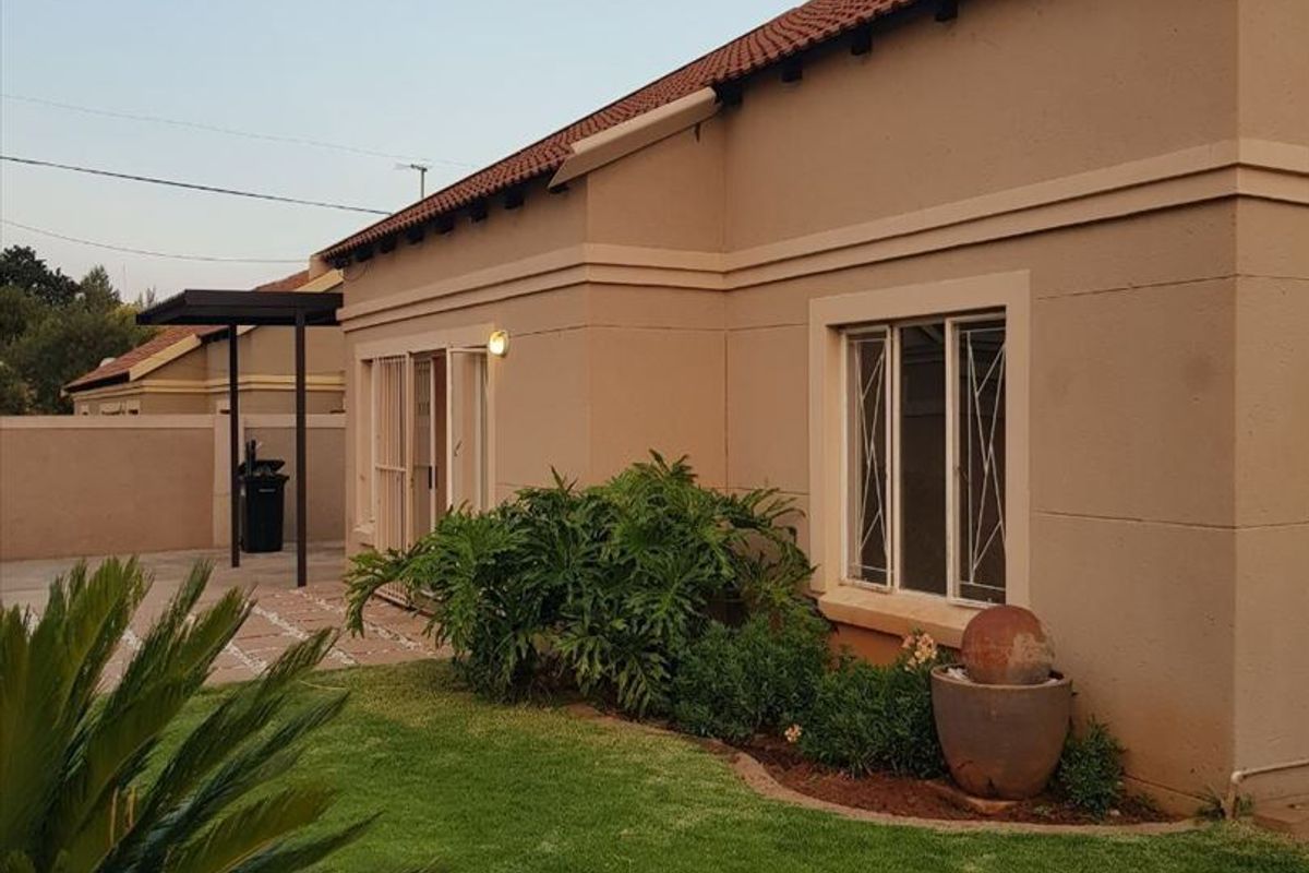 Rear view of the townhouse featuring a well-maintained garden, paved patio area, and secure window fittings.