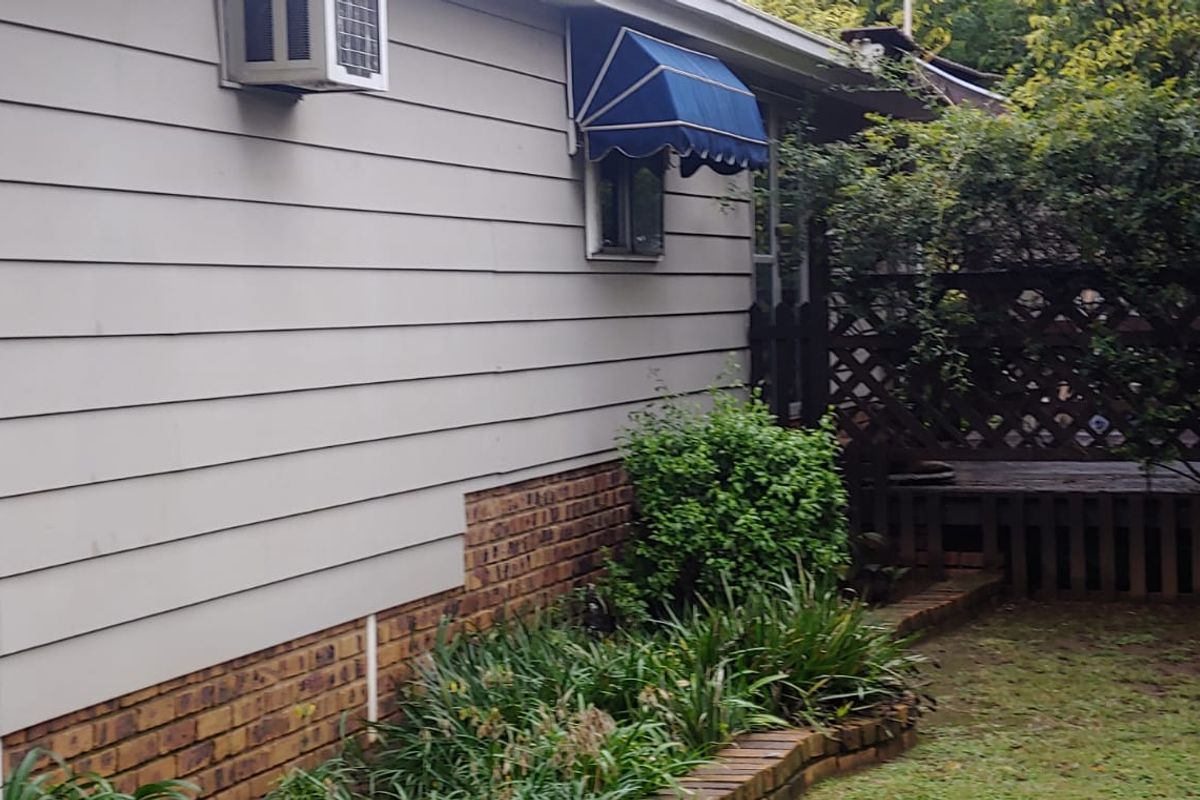 Rear exterior view of the property featuring brick foundation, siding, a window awning, and a small garden area with lattice screening.