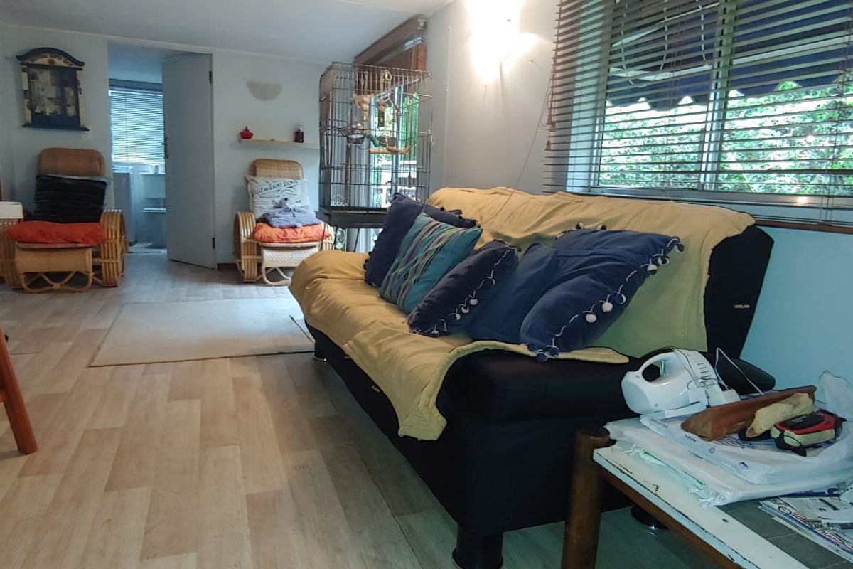 A living room featuring light-toned laminate flooring, wall-mounted lighting, and window blinds, offering a functional and neutral living space.