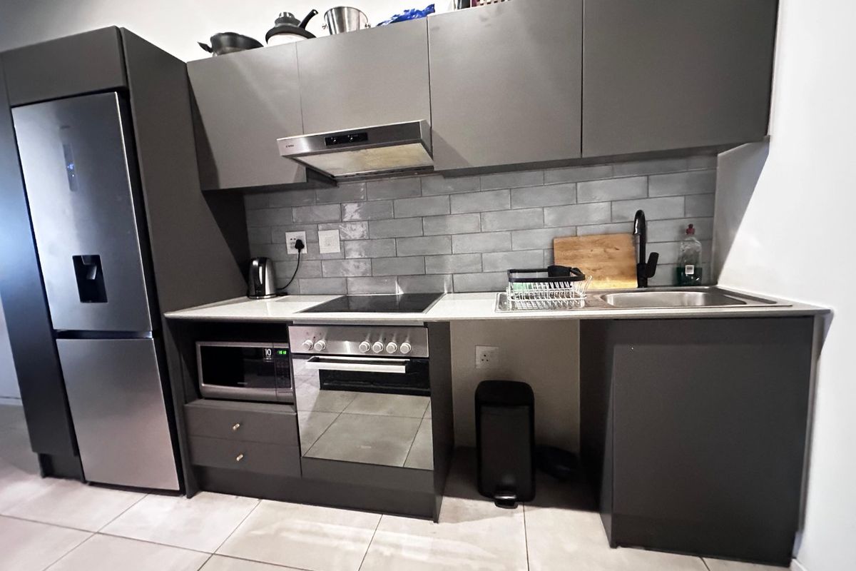 Modern kitchen featuring dark grey cabinetry, subway tile backsplash, integrated oven, electric hob, extractor fan, and stainless steel sink with tiled flooring.