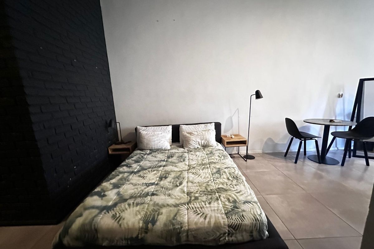 A bedroom featuring a dark exposed brick accent wall and large format floor tiles, offering a modern industrial aesthetic.