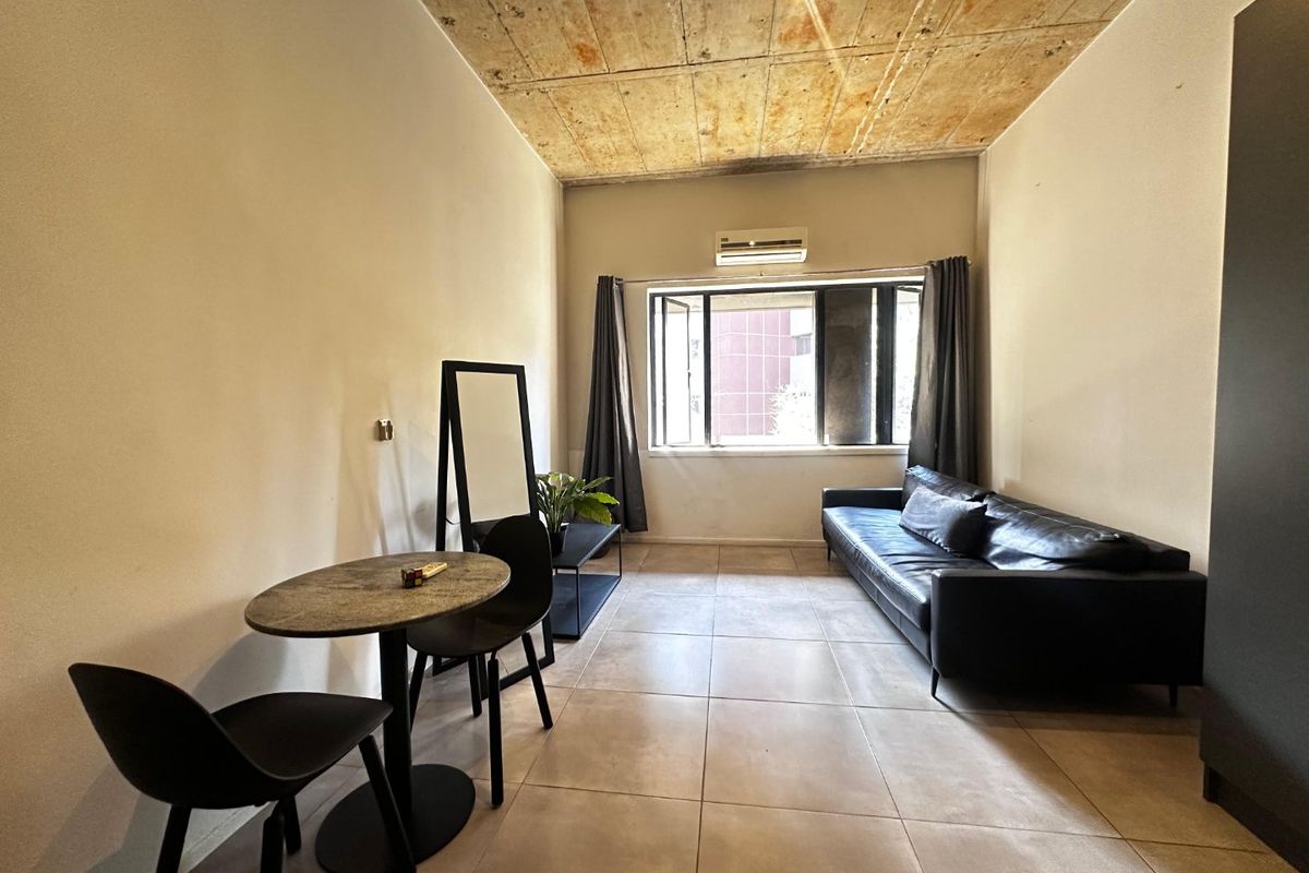 Living area featuring an industrial-style exposed concrete ceiling, large format floor tiles, and a wall-mounted air conditioning unit.