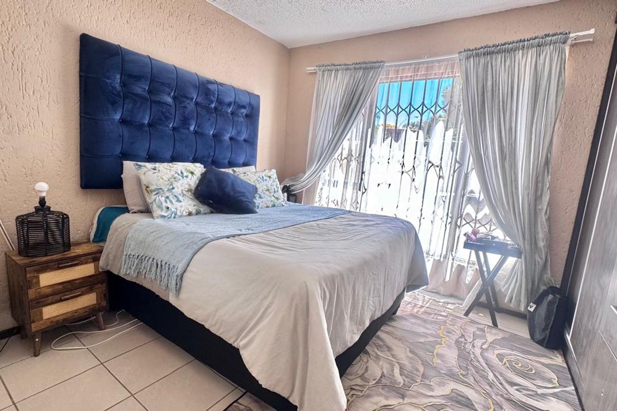 A bedroom featuring tiled flooring, textured walls, and a security gate over the window, providing a functional and secure living space.