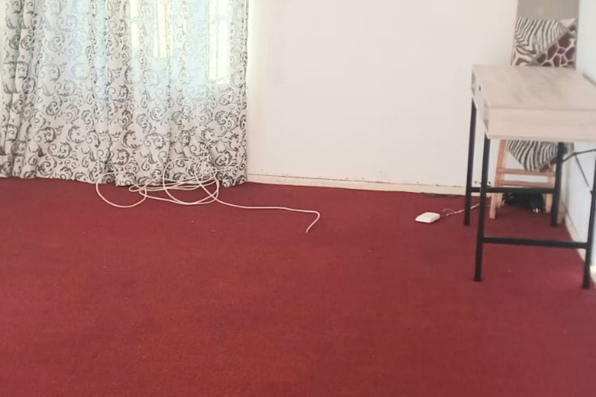 A sparsely furnished bedroom featuring red carpeting and a single window with curtains.