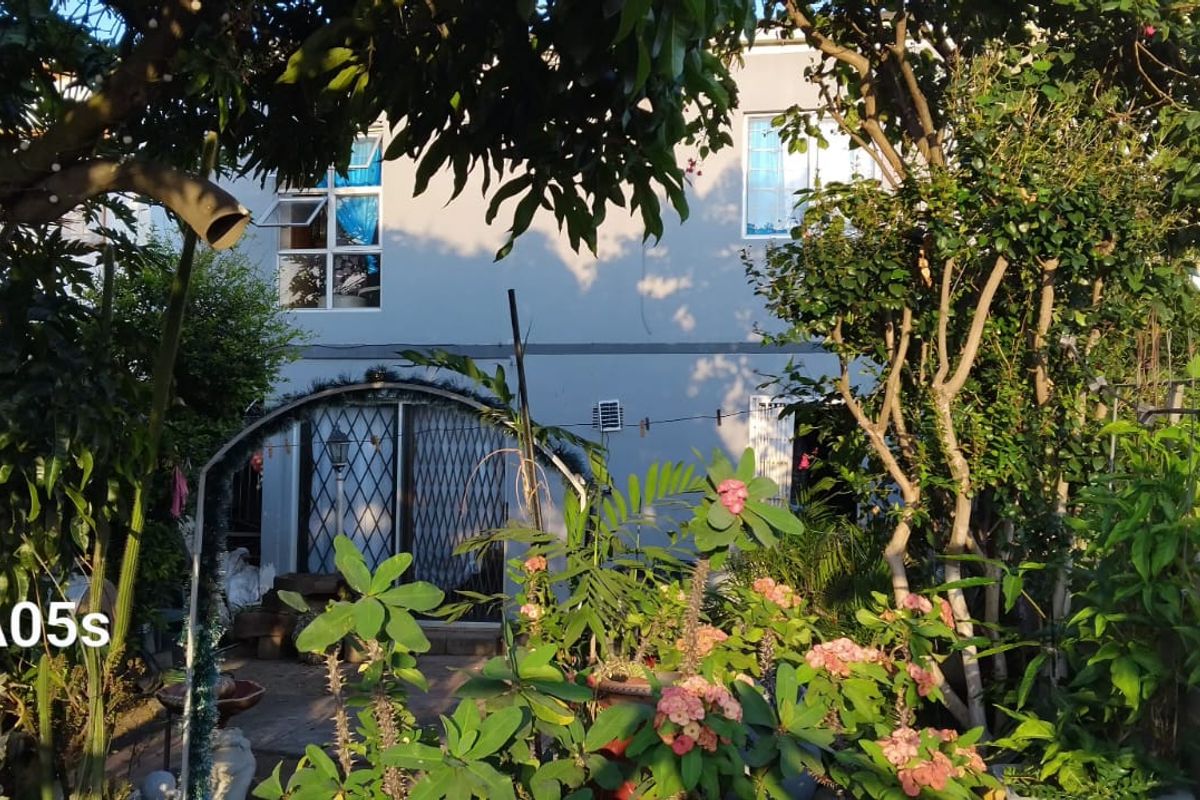 Rear view of the property featuring a garden area, security gate, and exterior wall finishes.